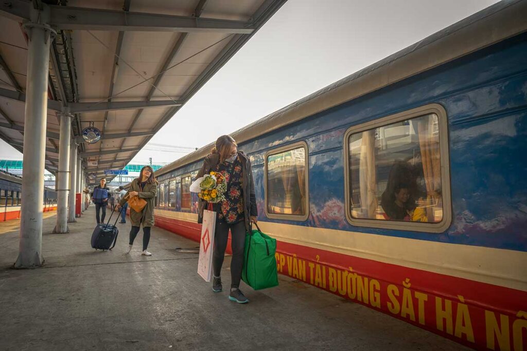 Passengers boarding a Reunification Express train at a station in Vietnam, showing the typical blue and red carriages used for long-distance train travel