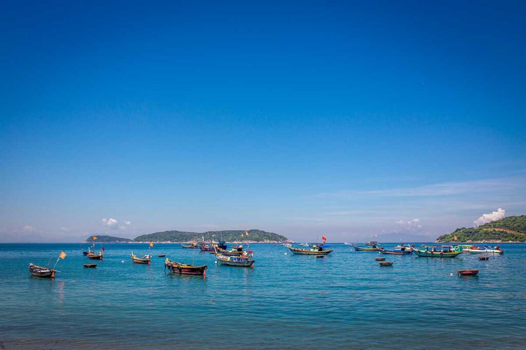 Colorful fishing boats floating on calm blue water near Hoi An during the dry months, when skies are clear and the sea is ideal for boat trips and beach visits.
