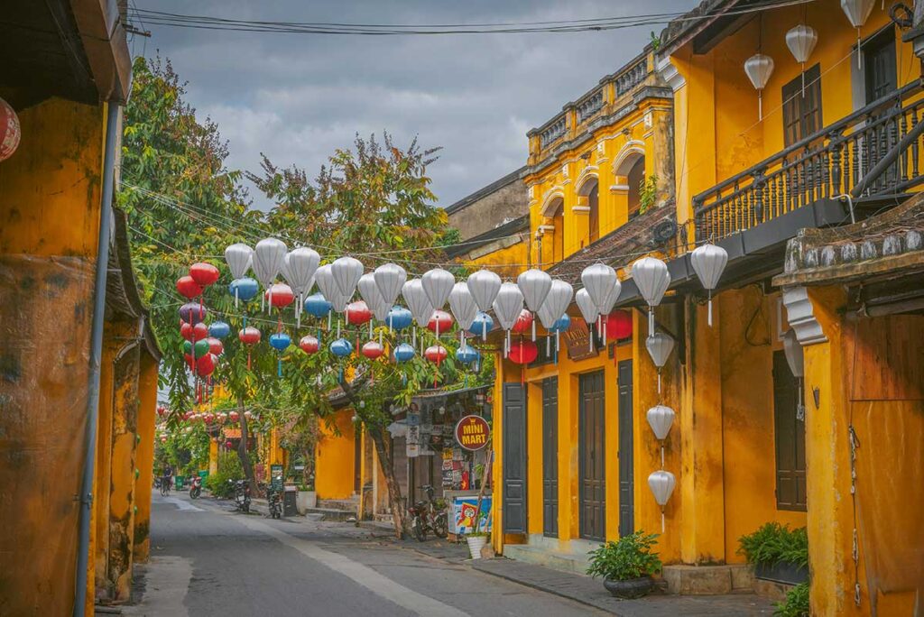 Empty street in Hoi An Ancient Town in December, with yellow heritage houses and colorful lanterns under cool, cloudy skies after the rainy season.