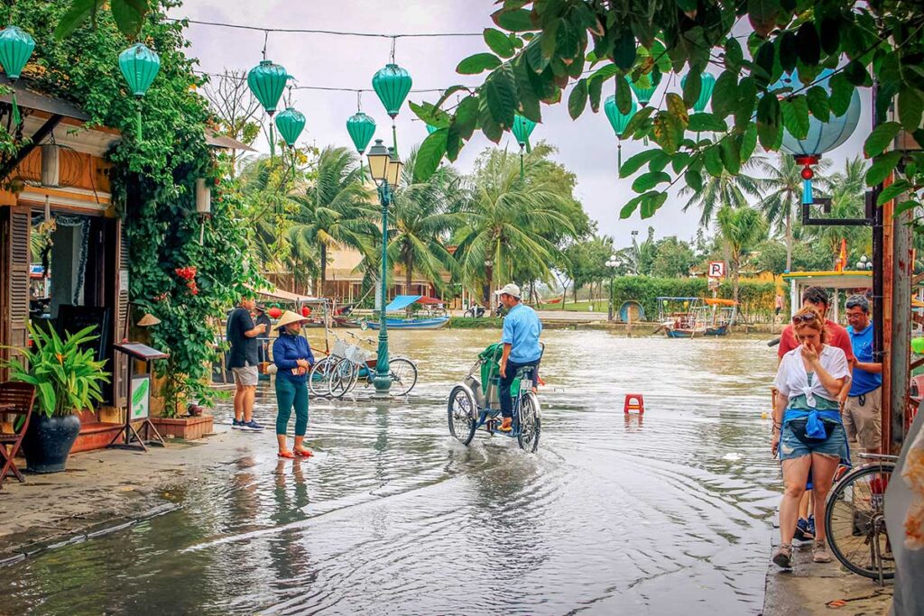 Flooded street in Hoi An Ancient Town with locals and tourists navigating shallow water, a common sight during heavy rains in central Vietnam.