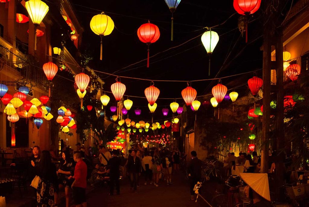 Old town street filled with hanging silk lanterns during the Hoi An Lantern Festival, with locals and tourists walking under the lights.