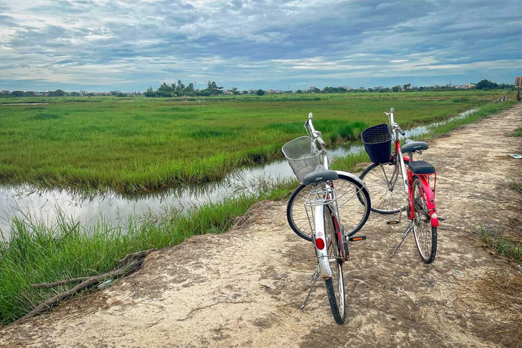 Bicycles parked on a rural path near Hoi An in October, with cloudy skies and lush rice fields reflecting the start of the rainy season in central Vietnam.