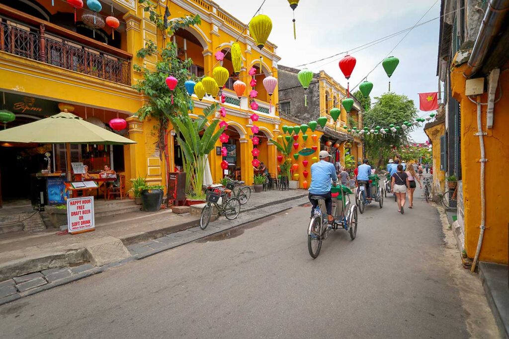 Cyclo drivers and tourists exploring Hoi An Ancient Town in October, when colorful lanterns brighten the streets despite frequent rain showers.