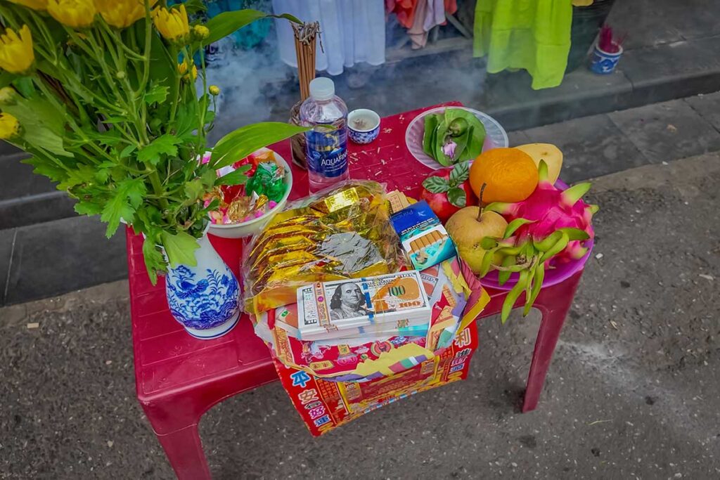 Close-up of Tet offerings in Hoi An, featuring incense, flowers, fruit, and symbolic paper money used to honor ancestors during the Lunar New Year.