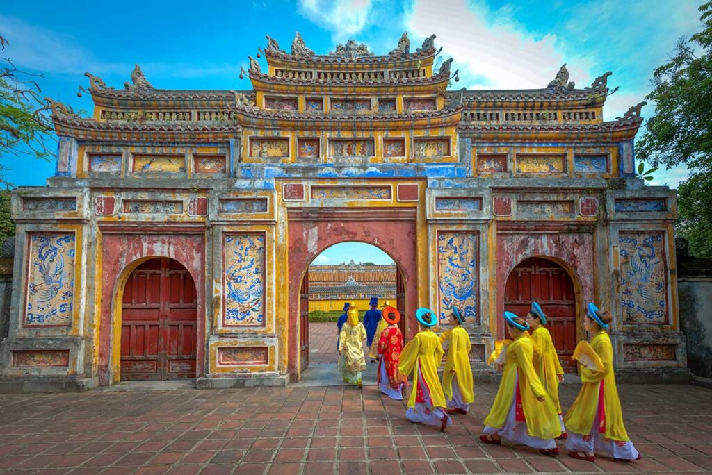 Hue in May - Woman in traditional clothes are walking through an ancient gate in Hue on a clear blue sky day