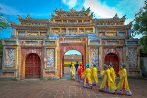 Hue in May - Woman in traditional clothes are walking through an ancient gate in Hue on a clear blue sky day
