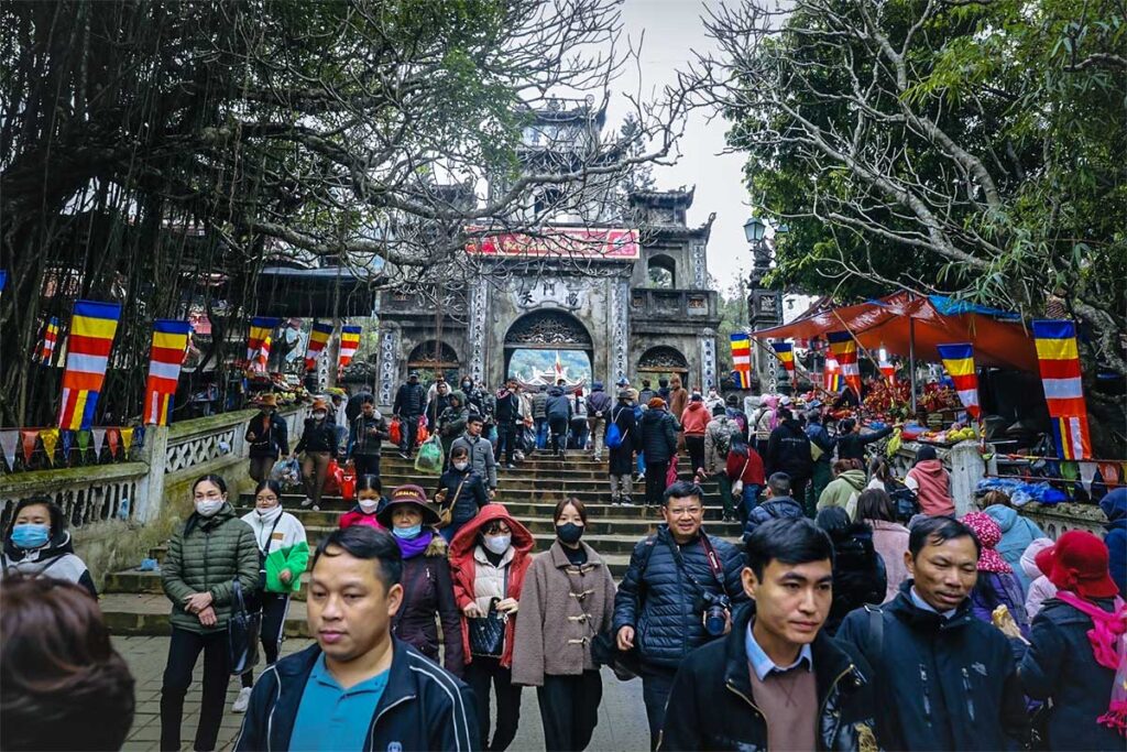 Stairs to a gate inside the Perfume Pagoda complex with lot of people walking and on the side of the walkway are a few small stalls selling snacks during Perfume Pagoda Festival
