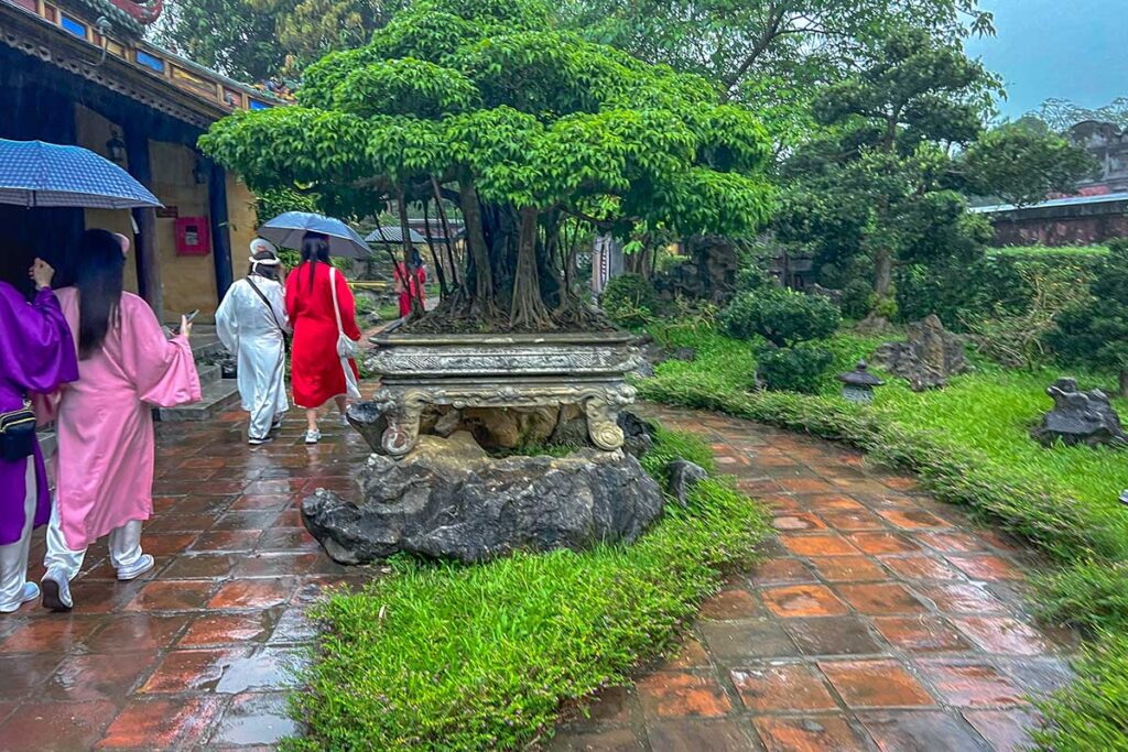Tourists walking at a historical building in Hue during rain with umbrellas