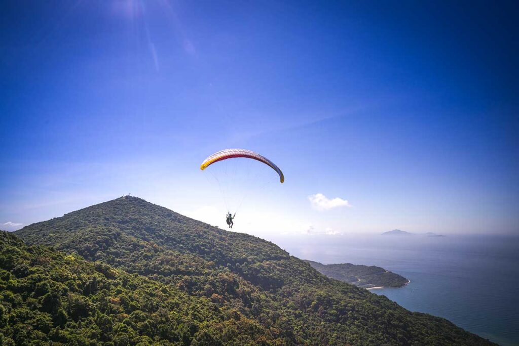 Tandem paragliding flight above Son Tra Peninsula, offering a stunning aerial view of Da Nang’s coastline, lush mountains, and the vast ocean.
