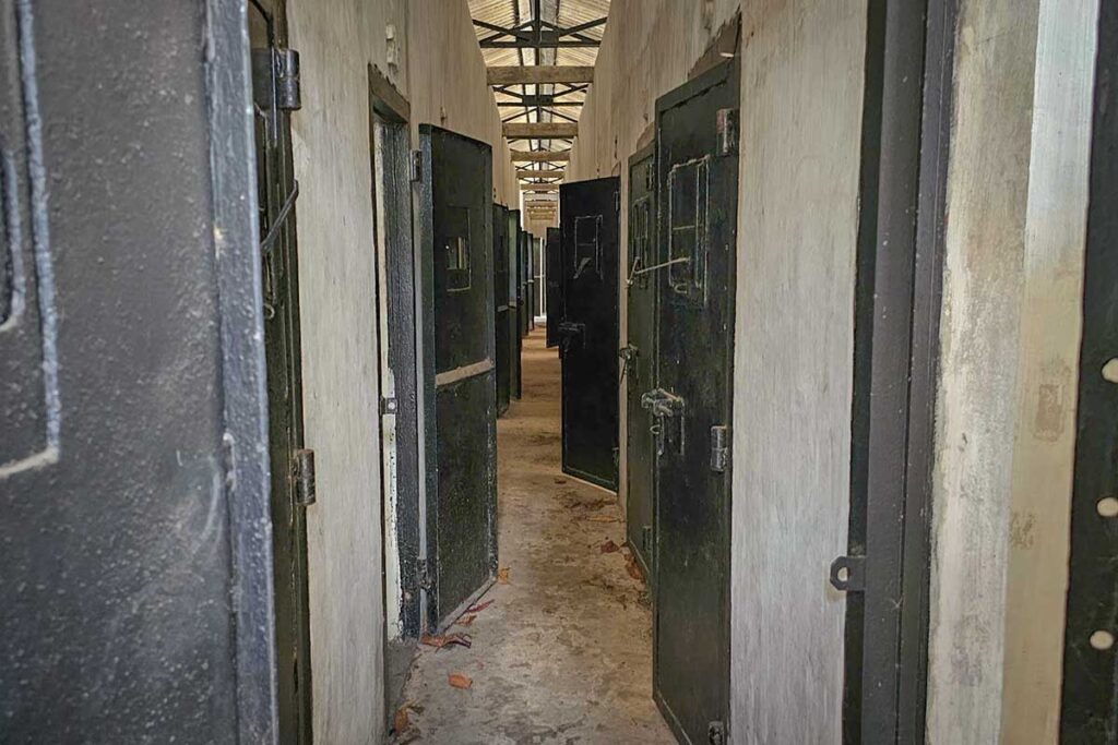 Narrow corridor lined with heavy metal doors inside the American Tiger Cages at Phu Binh Camp, illustrating the controlled and repetitive layout of this Vietnam War–era prison.
