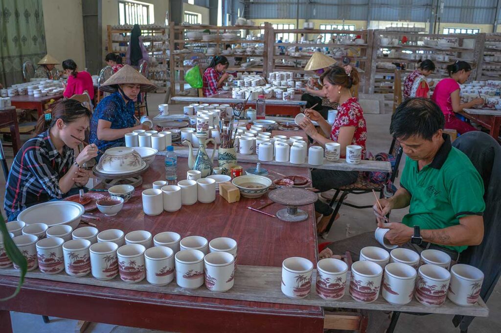 Lot of ceramic just made items located in a workshop with some local people working on new items at Chu Dau Ceramic Village