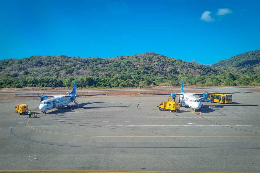 Small turboprop aircraft parked on the runway at Con Dao Airport surrounded by green hills and tropical landscape