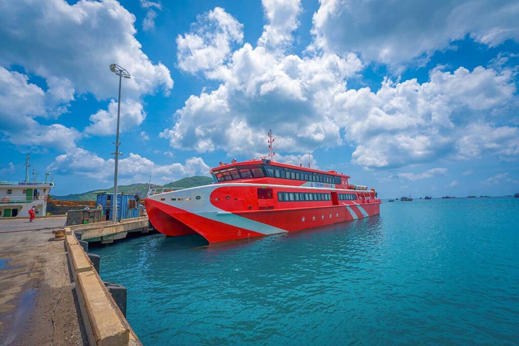 Red high-speed Con Dao Express ferry docked at the pier with clear blue water and island scenery in the background