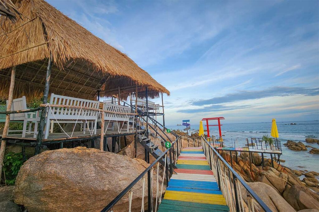 Seaside bamboo hut café with colorful walkway overlooking rocky coast of Cu Lao Xanh.