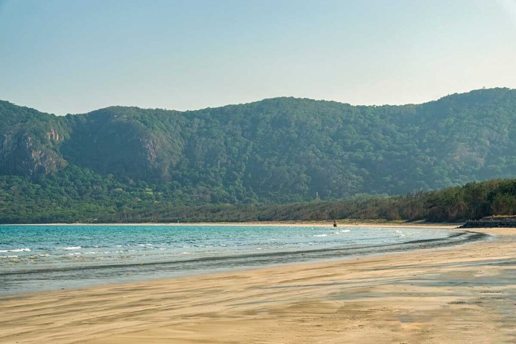 Long coastline of Dong Beach in Con Dao with light waves, sandy shore, and forest-covered mountains creating a peaceful coastal landscape.
