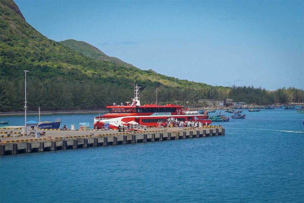 High-speed ferry arriving at Con Dao harbor with clear blue water and green mountains in the background