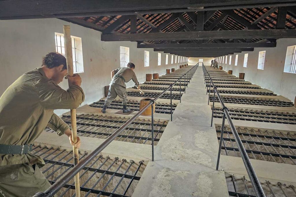 Interior view of the French Tiger Cages at Con Dao prison, with guards standing on a walkway above iron-barred cells used to isolate prisoners below.