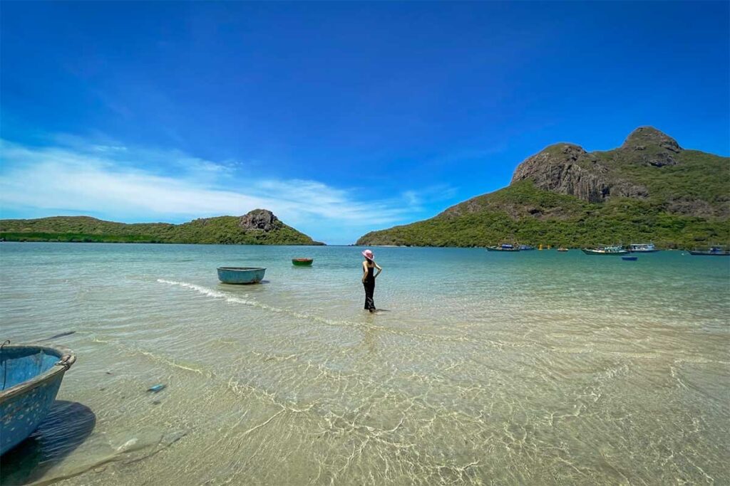 Shallow clear water at Hong Dam Beach in Con Dao with a person standing in the sea and traditional round basket boats floating nearby.