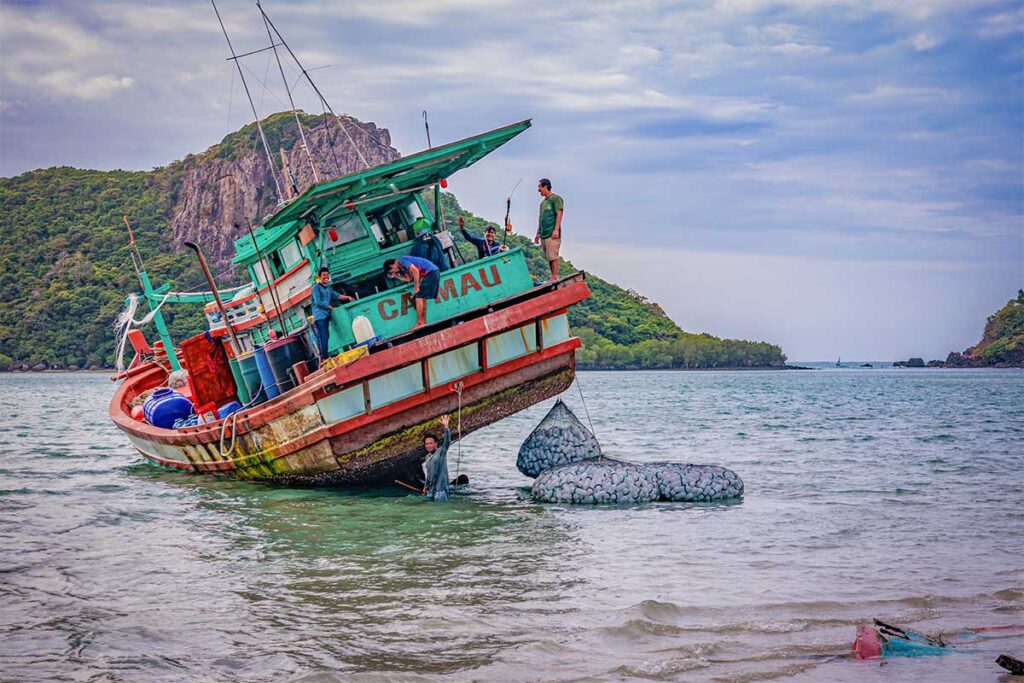 Local fishermen working beside a colorful wooden boat near Hong Dam Island in Con Dao, unloading catch in shallow coastal waters.