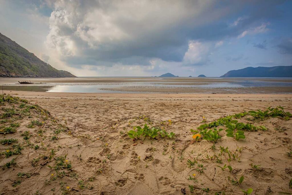 Expansive sandy area at Lo Voi Beach in Con Dao during low tide with distant islands, cloudy sky, and footprints in the foreground.