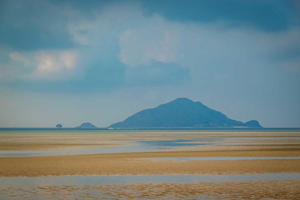 Low tide at Lo Voi Beach in Con Dao revealing wide sand flats and shallow water with a mountain island visible on the horizon.
