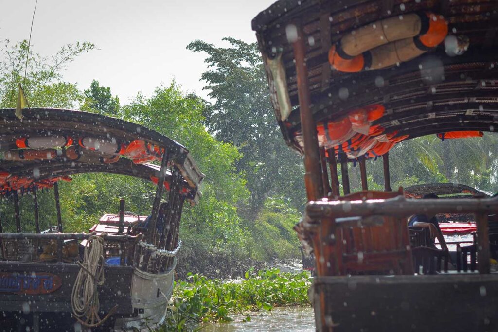 Tour boats on a narrow canal with raindrops falling, illustrating the atmosphere of a boat tour in the Mekong Delta during rainy season.