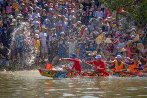 Crowds cheer a colorful dragon boat race splashing across the river, reflecting festive rainy-season energy in the Mekong Delta in September.