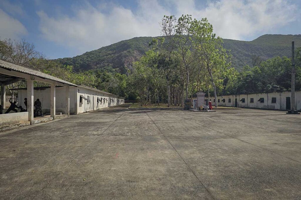 Wide open courtyard at Phu An Prison on Con Dao, surrounded by low prison buildings and mountains in the background, showing the scale of the prison complex.