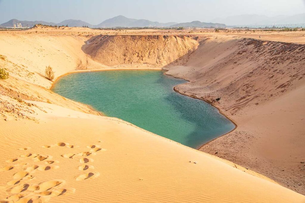 Natural lake framed by the golden slopes of Phuong Mai Sand Dunes, creating a striking contrast between turquoise water and arid sand