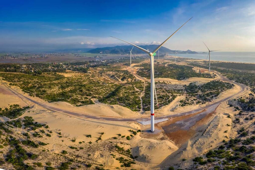 Aerial view of giant wind turbines rising above Phuong Mai Sand Dunes, overlooking the coastline and hills of Quy Nhon’s Phuong Mai Peninsula