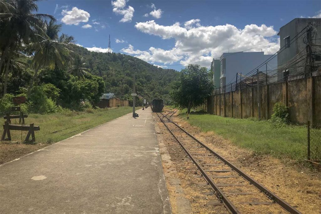 Platform and single track at Quy Nhon Railway Station surrounded by greenery and low buildings, emphasizing its quiet atmosphere.