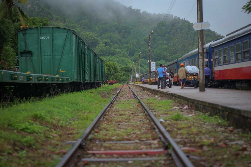 Railway tracks at Quy Nhon Station with passenger and freight cars, highlighting the branch line connection through green hills near the city.