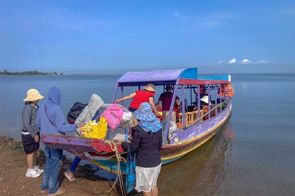 A group of Vietnamese stepping onto a wooden boat that is used for boat tours on Tri An Lake