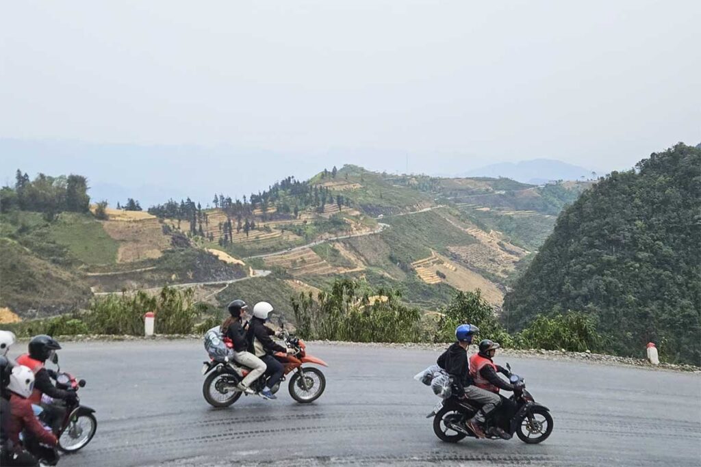 Side view of three Easy Rider motorbikes with tourists on a winding Ha Giang mountain road