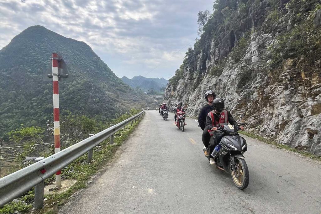 Group of tourists and Easy Riders riding motorbikes on a scenic Ha Giang Loop route