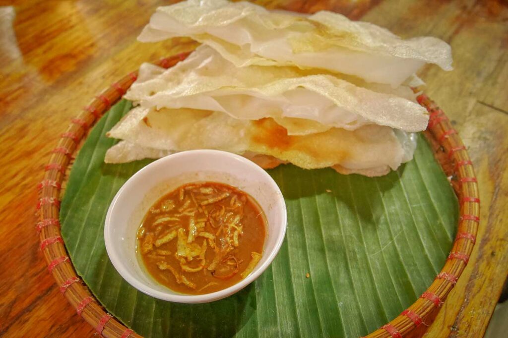 Traditional bánh đập in Hoi An, a crispy rice cracker layered with soft rice paper, served with a bowl of savory dipping sauce topped with fried shallots