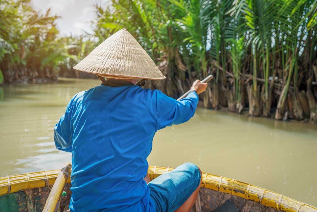 Local guide rowing through nipa palms in a round bamboo basket boat – traditional basket boat tour in Hoi An countryside.