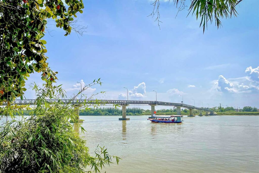 “Wooden tour boat sailing along the Thu Bon River near Cam Kim Island, offering peaceful river cruises from Hoi An