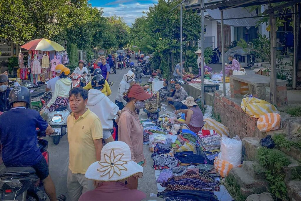 Busy street market scene at Cam Kim Market, locals shopping for fresh produce, clothes, and household goods