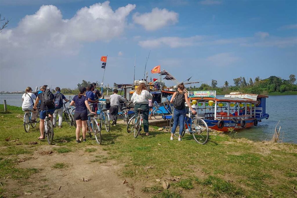 Tourists with bicycles boarding a wooden boat for a combined cycling and boat tour on Cam Kim Island, Hoi An