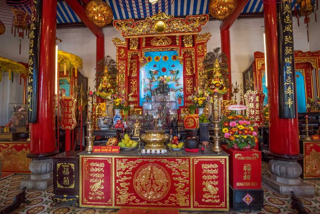 Interior shrine at Cantonese Assembly Hall Hoi An with golden statues, incense spirals, and symbolic decorations.
