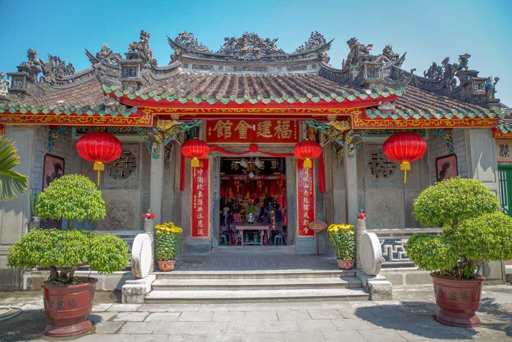 Front façade of Cantonese Assembly Hall Hoi An with red lanterns, detailed carvings, and tiled roof.