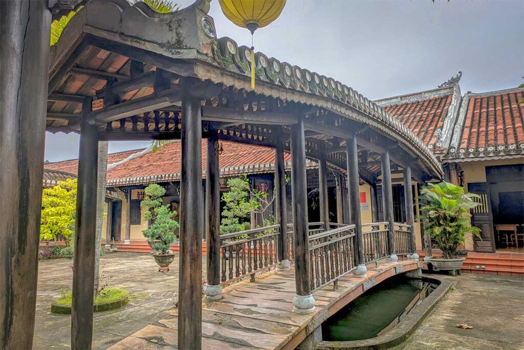 Wooden bridge with tiled roof over a courtyard pond inside Chuc Thanh Pagoda in Hoi An