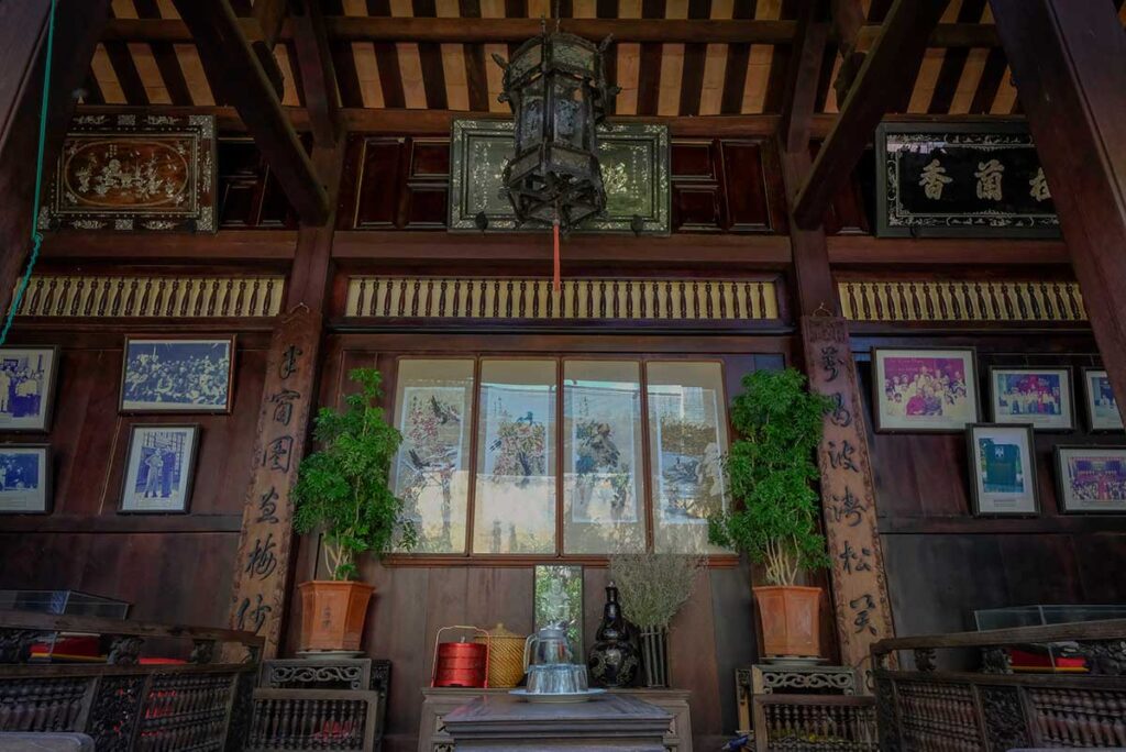 Living space inside Duc An Old House in Hoi An with carved wooden chairs, calligraphy panels, and framed family photographs.