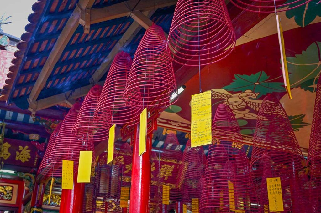 Red spiral incense coils with prayer notes hanging from the ceiling inside Hoi An’s Fujian Assembly Hall.