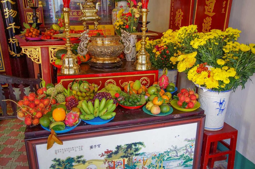 Colorful fruit offerings and fresh flowers placed at the altar inside Phuc Kien Assembly Hall, Hoi An.