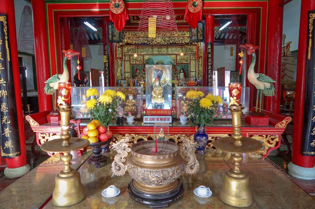 Worship altar with golden incense burner, floral offerings, and deity statues inside Hoi An’s Fujian Assembly Hall.