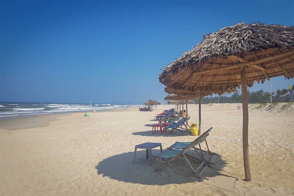 Golden sands of Ha Thanh Beach in Tam Ky, Quang Nam, with palm-thatched umbrellas and beach chairs facing the waves.