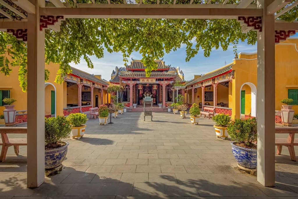 Courtyard view of Hai Nam Assembly Hall in Hoi An with yellow walls, bonsai planters, and traditional Chinese-style roof tiles.