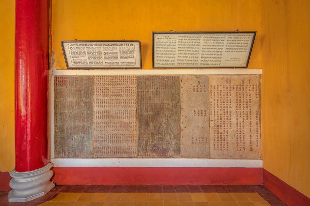 Memorial tablets at Hai Nam Assembly Hall listing 108 Hainan merchants lost at sea, with bilingual history panels on the wall.